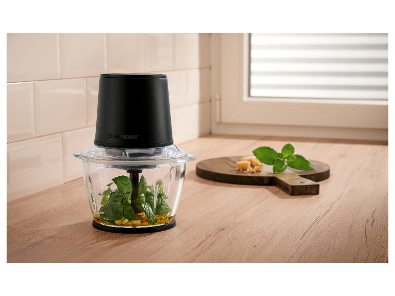 Hachoir avec basilic, huile et noix, à côté de fromage et menthe sur une planche en bois.