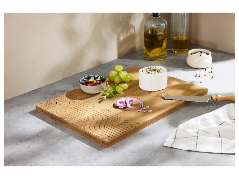 Une planche à découper en bois avec du fromage, des raisins, de l'oignon rouge et un petit bol de confiture.