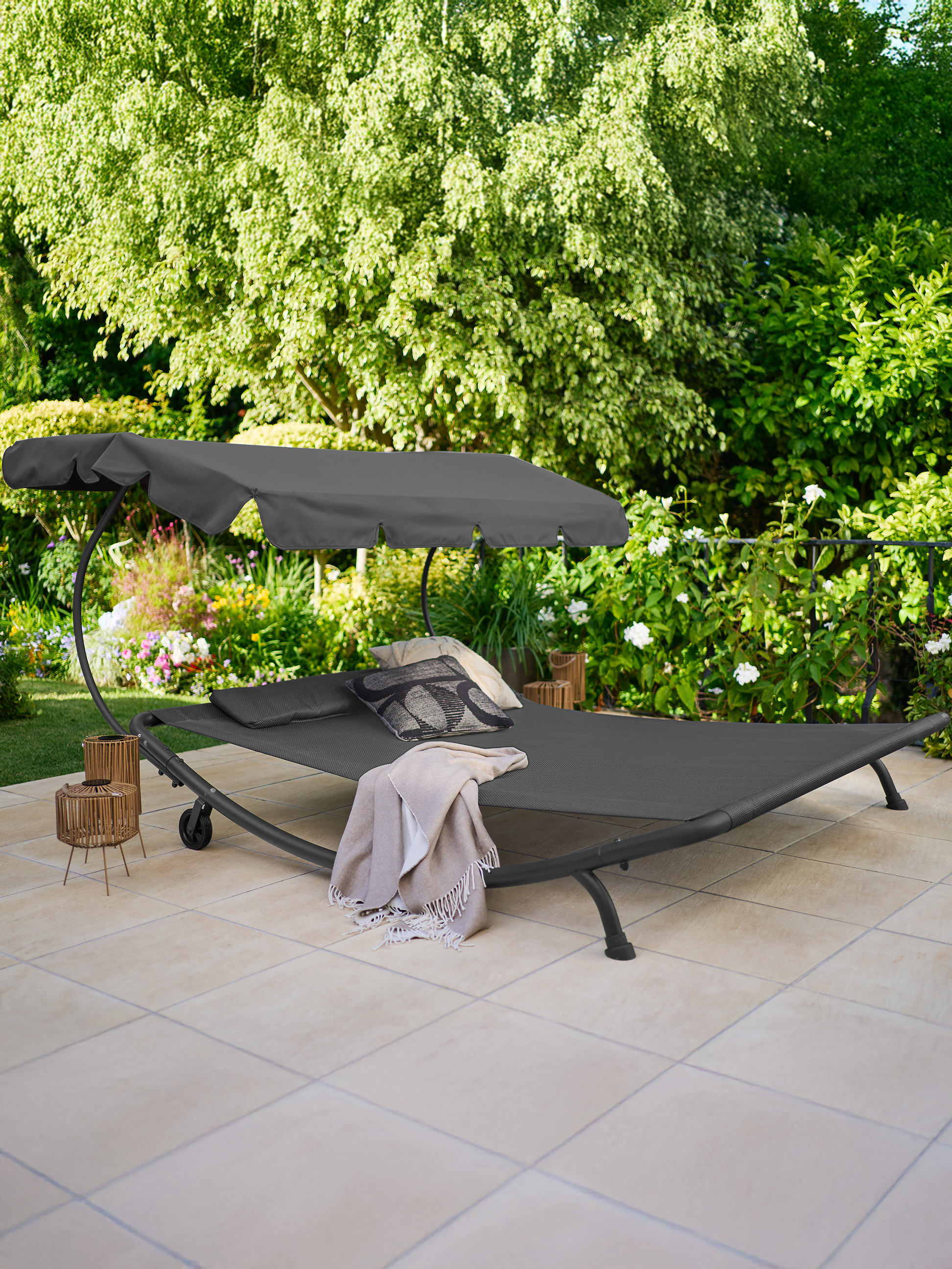 Bain de soleil de jardin avec auvent et coussins sur une terrasse, entouré de verdure.