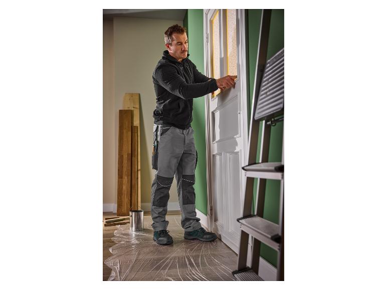 Homme en tenue de travail préparant une porte pour la peinture.