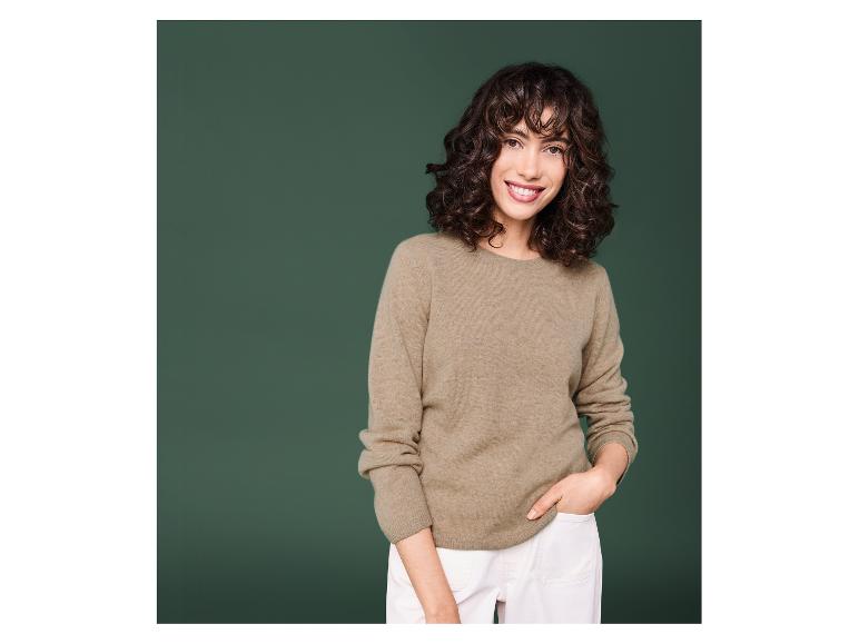 Une femme portant un pull beige et un pantalon blanc.
