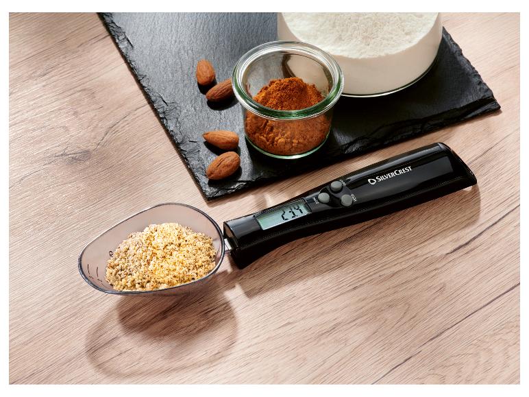 Cuillère doseuse numérique SilverCrest avec amandes, farine et épices sur une planche en ardoise.