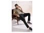 Homme en t-shirt beige et pantalon noir assis dans un fauteuil.