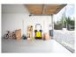 Garage avec balayeuse jaune, vélo, outils de jardin et tables pliantes.