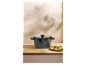 Une casserole foncée avec un couvercle en verre et une portion de légumes rôtis dans une assiette.
