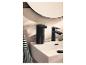 Distributeur de savon noir et robinet sur lavabo blanc, avec miroir rond en arrière-plan.