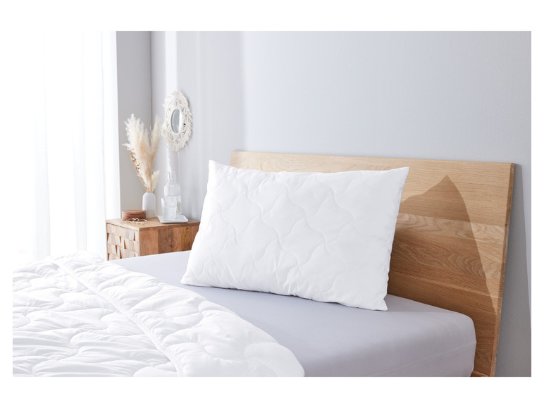 Une couette et un oreiller blancs sur un lit avec une tête de lit en bois.