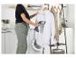 Personne défroissant une chemise blanche dans une buanderie avec étendoir et lave-linge.