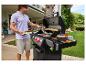Homme grillant des hamburgers sur un barbecue extérieur, avec pains et légumes.