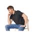 Un homme pensif assis sur une chaise, portant un polo noir et un jean.