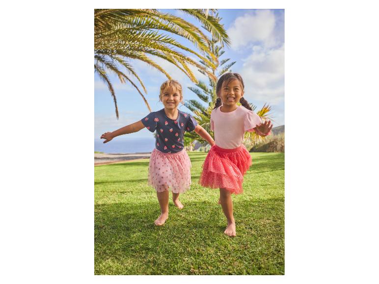 Deux filles en hauts imprimés fraises et jupes en tulle courant sur l'herbe.