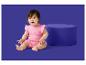 Un bébé en barboteuse rose à motif soleil assis à côté d'un pouf bleu.