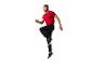 Un homme en t-shirt rouge et pantalon de jogging noir saute.
