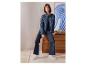 Femme en jean large ESMARA® et veste en jean assise sur une commode.