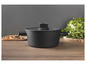 Une casserole noire avec un couvercle sur une table en bois.