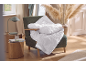 Couette blanche sur un fauteuil, table d'appoint en bois avec lampe et verre.