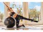 Une femme en tenue de sport s'entraîne sur un tapis avec un ballon de gymnastique.