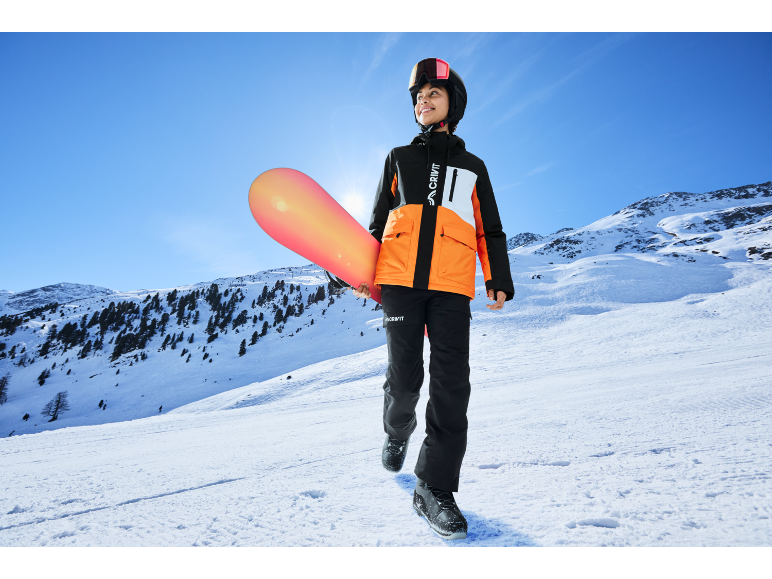 Jeune personne en veste et pantalon de ski avec snowboard sur une montagne enneigée.