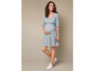 Une femme enceinte porte une robe bleue à fleurs et des baskets blanches.