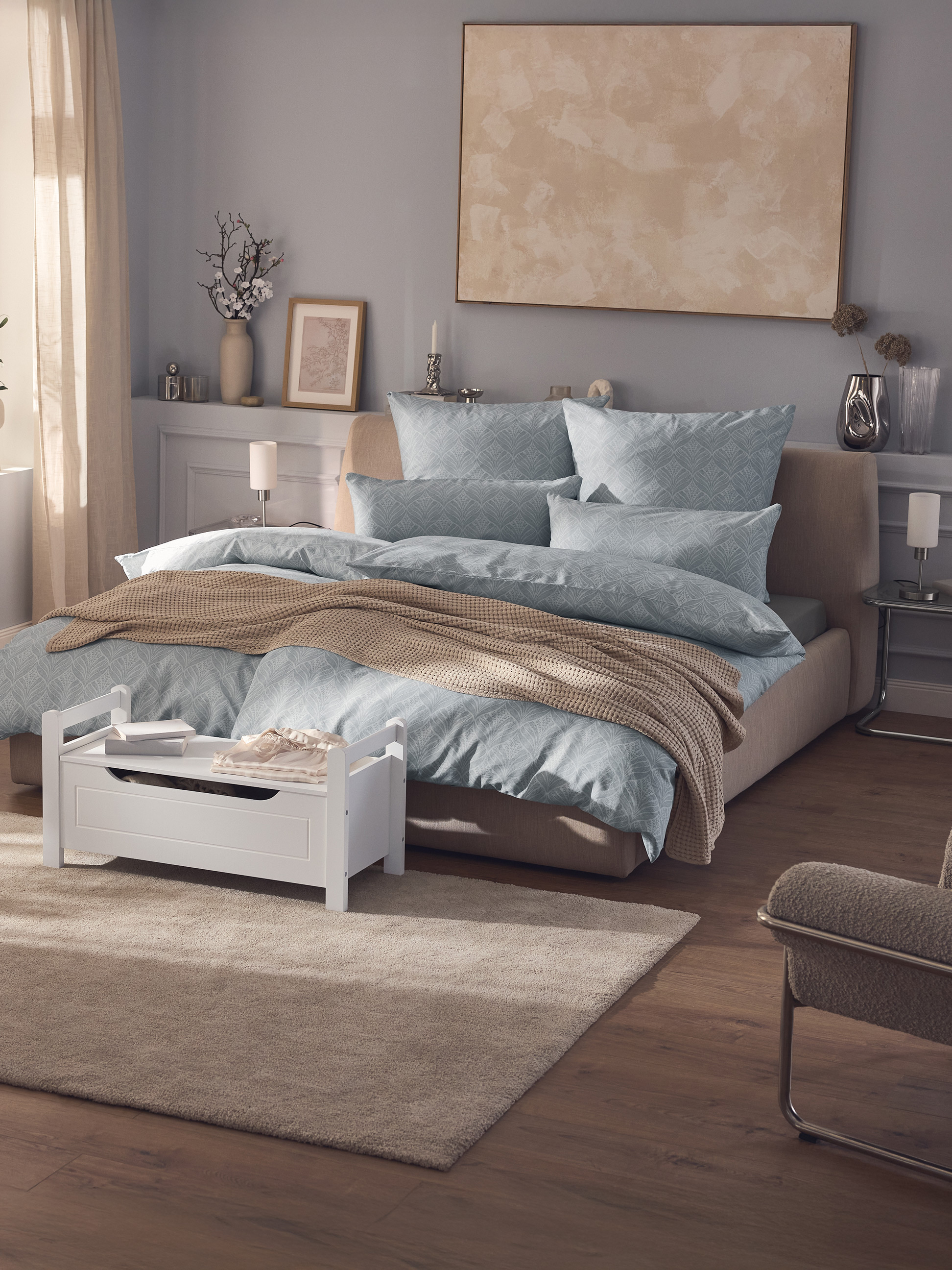 Chambre à coucher moderne avec lit double, parure de lit bleue à motifs, jeté de lit beige et coffre de rangement blanc.