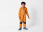 Un garçon porte une combinaison orange avec un éléphant et des bottes bleues.