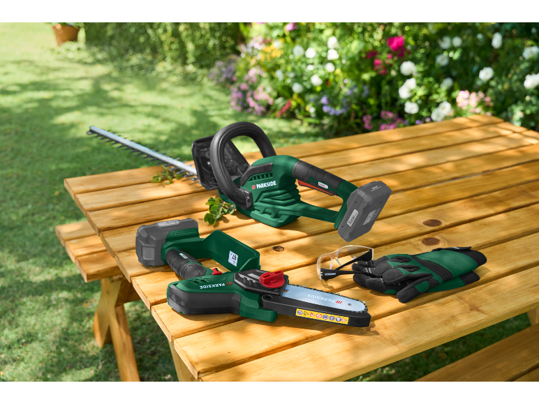 Taille-haie et scie d'élagage sans fil sur une table en bois dans le jardin avec lunettes et gants.
