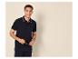 Homme souriant en polo bleu marine et pantalon, tenant des lunettes.