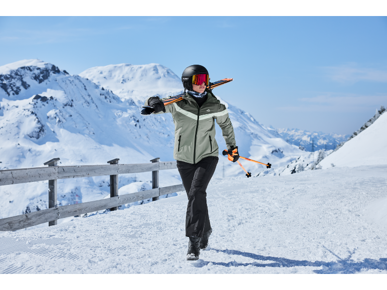 Skieuse en veste et pantalon de ski avec skis et bâtons sur une piste de ski