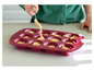 Une main remplit un moule à muffins en silicone rouge avec de la pâte.