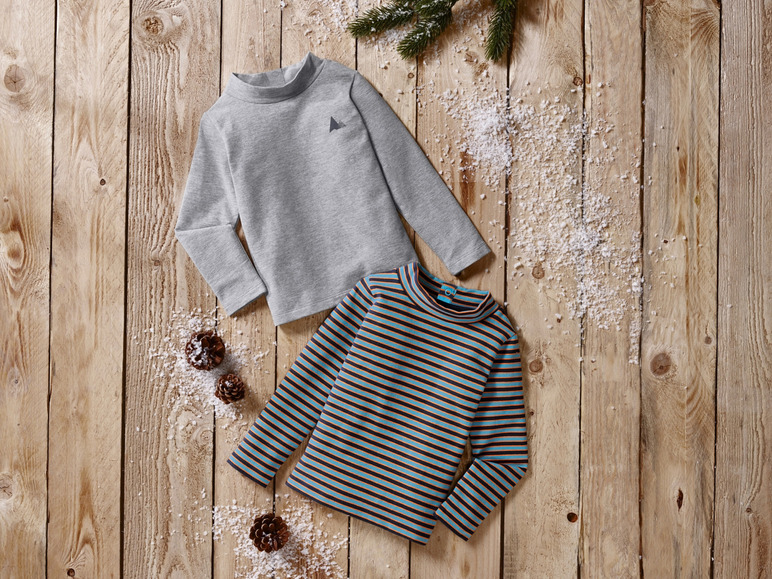 Deux t-shirts à manches longues, un gris et un rayé, sur un fond en bois.