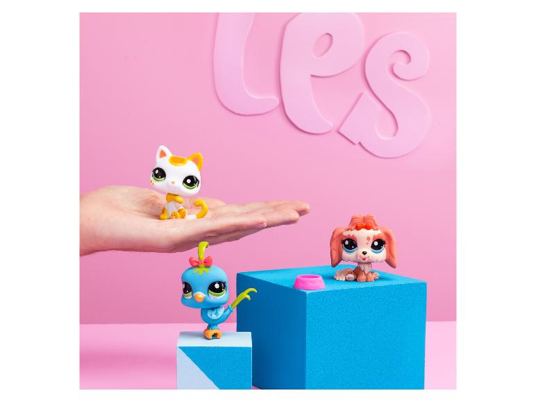 Trois jouets colorés Littlest Pet Shop, dont un chat, un chien et un oiseau, sur des blocs roses et bleus.