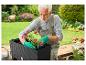 Un homme plante des fleurs dans un pot en osier noir de la marque Westcott Home.