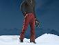 Un homme en pantalon de ski rouge et un casque noir devant les montagnes.