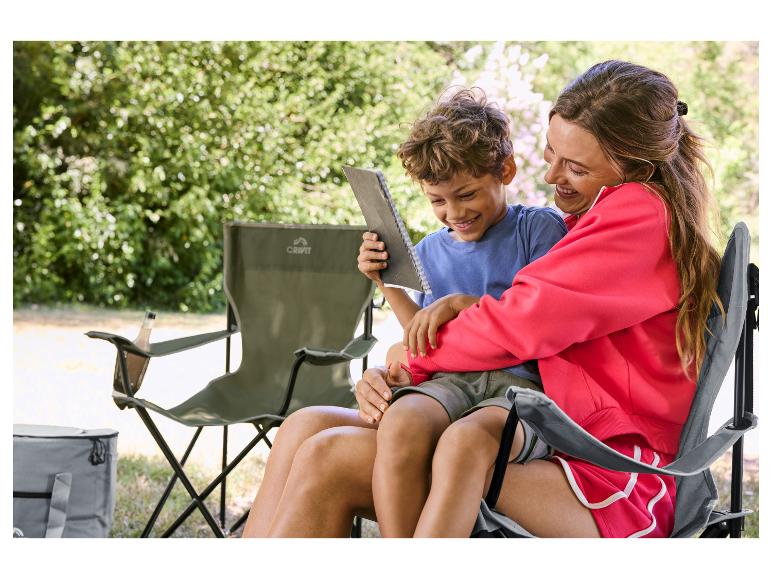 Femme et enfant assis sur des chaises de camping, lisant un livre en extérieur.