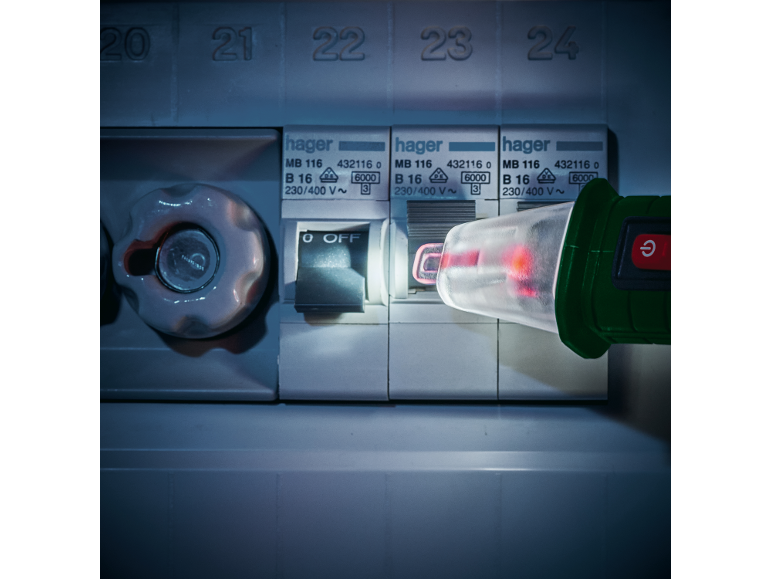 Un électricien utilise un testeur de tension Hager pour vérifier un tableau électrique.