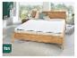 Lit en bois avec matelas et surmatelas blancs, dans une chambre avec vue sur la verdure.