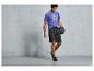 Un homme en t-shirt bleu et short noir tenant un ballon de sport.