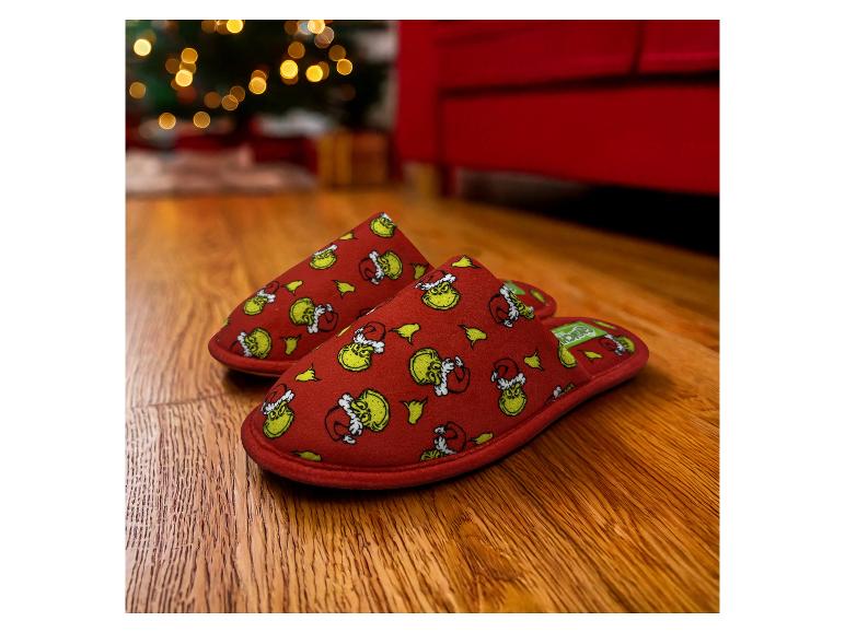 Pantoufles rouges à motif Grinch sur un parquet, avec des lumières de Noël en arrière-plan.