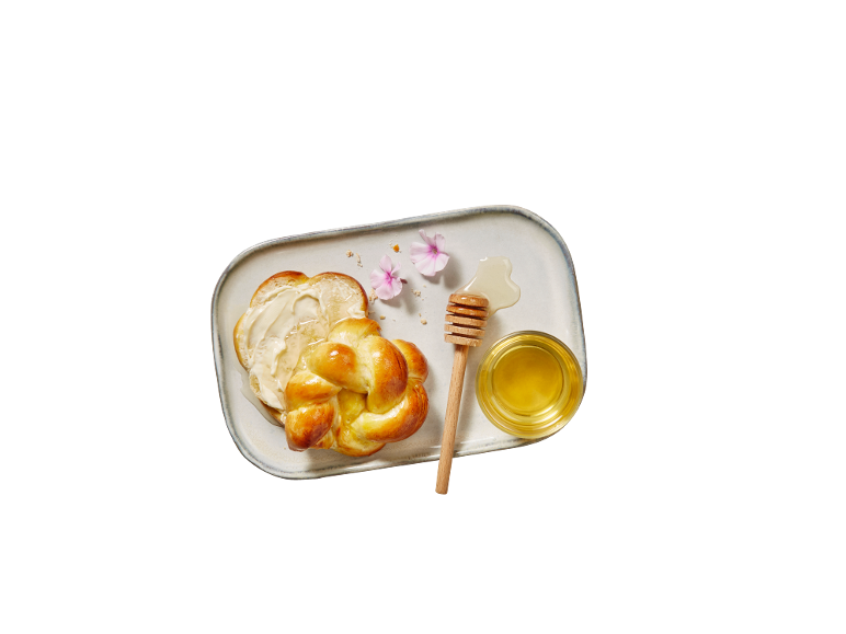 Pain tressé avec du fromage frais et du miel sur un plateau blanc.
