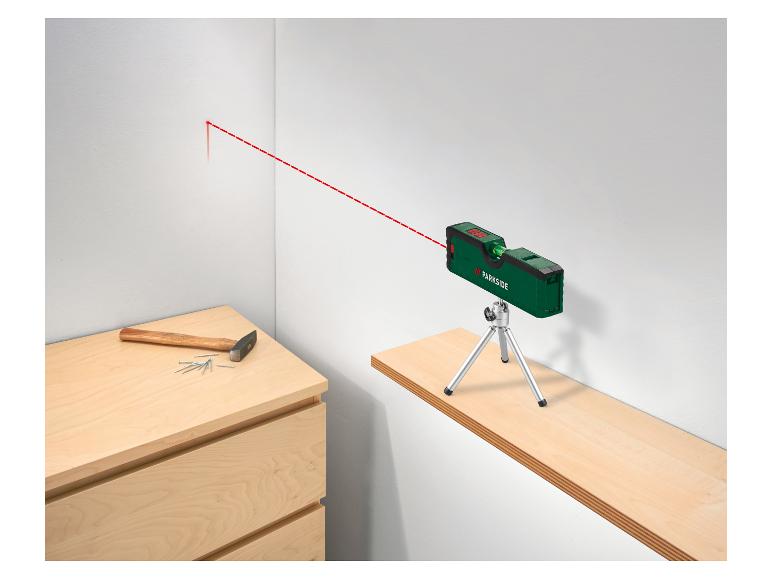 Niveau laser vert avec trépied projetant une ligne rouge sur un mur, avec marteau et clous.