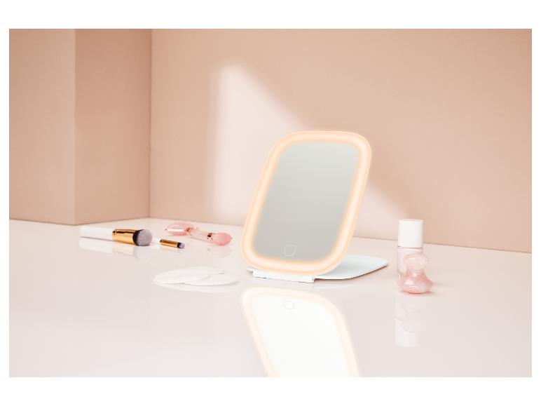 Miroir de maquillage lumineux avec pinceaux, cotons et vernis à ongles sur une coiffeuse.