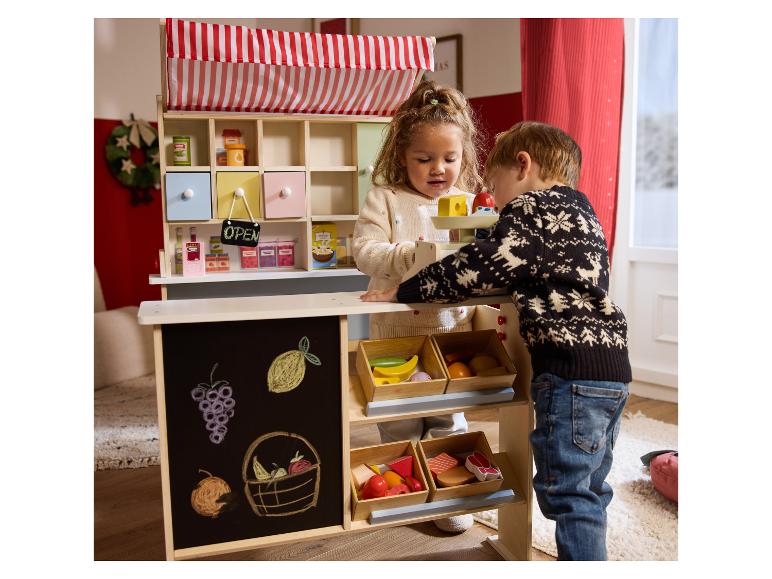 Deux enfants jouent avec un stand de marché miniature avec fruits, légumes et une balance.