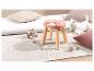 Un tabouret en bois rose avec un motif arc-en-ciel sur un tapis blanc.