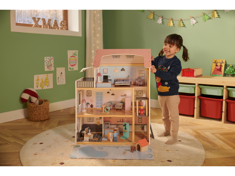 Une enfant joue avec une grande maison de poupées en bois dans une pièce festive.