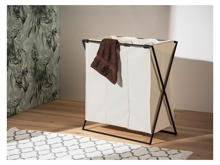 Un panier à linge pliable à trois compartiments, en tissu beige et structure noire, posé sur un sol en bois.