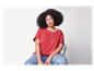 Une femme aux cheveux bouclés est assise sur une chaise, vêtue d'un t-shirt rouge et d'un jean.