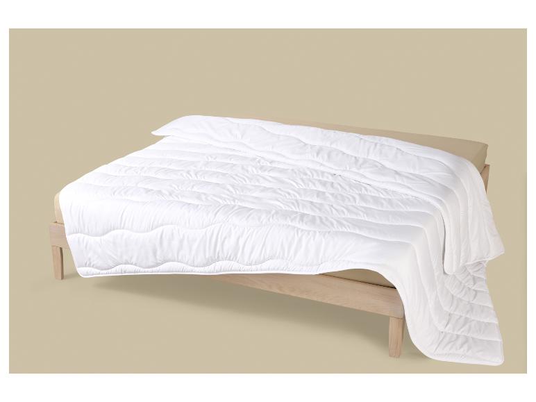 Couette blanche matelassée sur un cadre de lit en bois clair avec un drap beige.