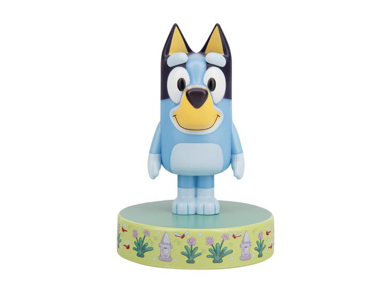 Figurine de chien bleu de dessin animé sur une base verte avec un thème de jardin.