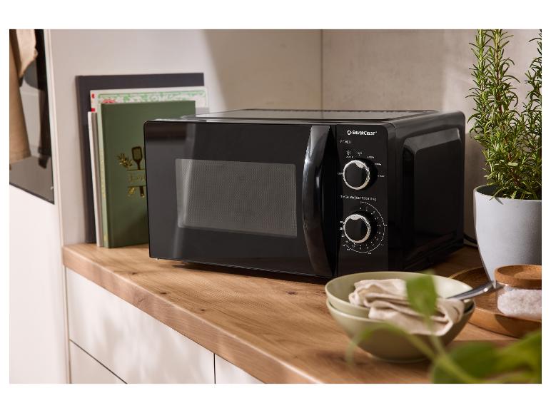 Micro-ondes Silvercrest noir sur un comptoir en bois avec des livres de cuisine et une plante.