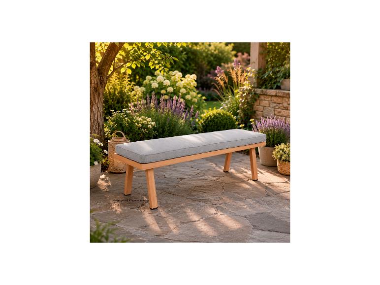 Banc de jardin en bois avec coussin gris sur une terrasse en pierre, entouré de plantes et de fleurs luxuriantes.